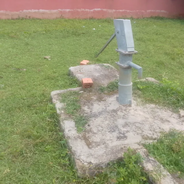 A hand-operated borehole hand pump on a concrete apron in a Nigerian community. Openly licensed photograph by NigerianScribe.